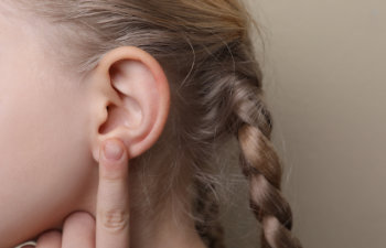 Child with a braided hairstyle pressing finger to ear.