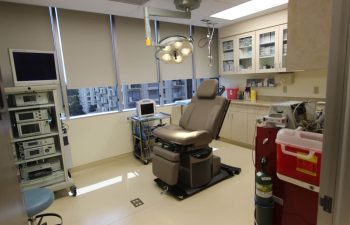 A modern operating room equipped with an adjustable surgical chair, overhead lights, and various medical machines.