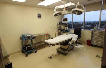 An empty operating room equipped with a surgical table, overhead lights, and various medical machines.