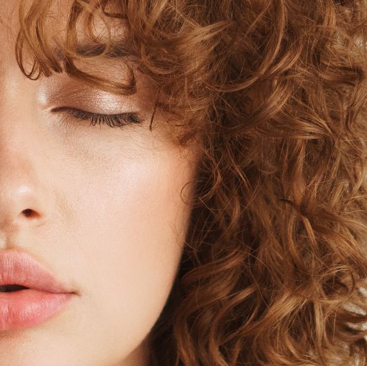 Close-up of a person with curly hair, closed eye, and natural makeup.