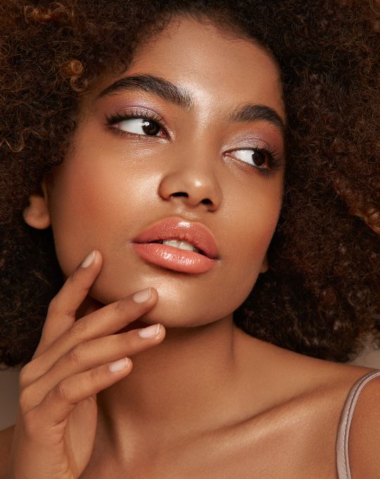 A woman with curly hair looking upwards while gently touching her chin with a soft expression.