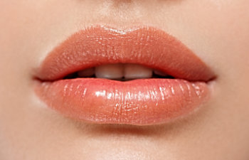 Close-up of a person’s lips slightly parted, featuring glossy pink lipstick.