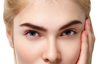 Close-up of a person with light hair touching their face. The image emphasizes their eyes, eyebrows, and smooth skin.
